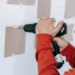 Close-up of hands using a drill on wall in home improvement setting.