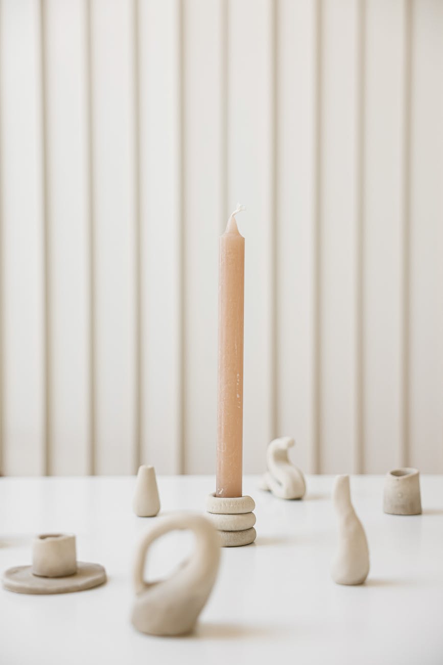 A minimalistic still life of a clay candle holder and wax candle on a white table, showcasing elegant craftsmanship.