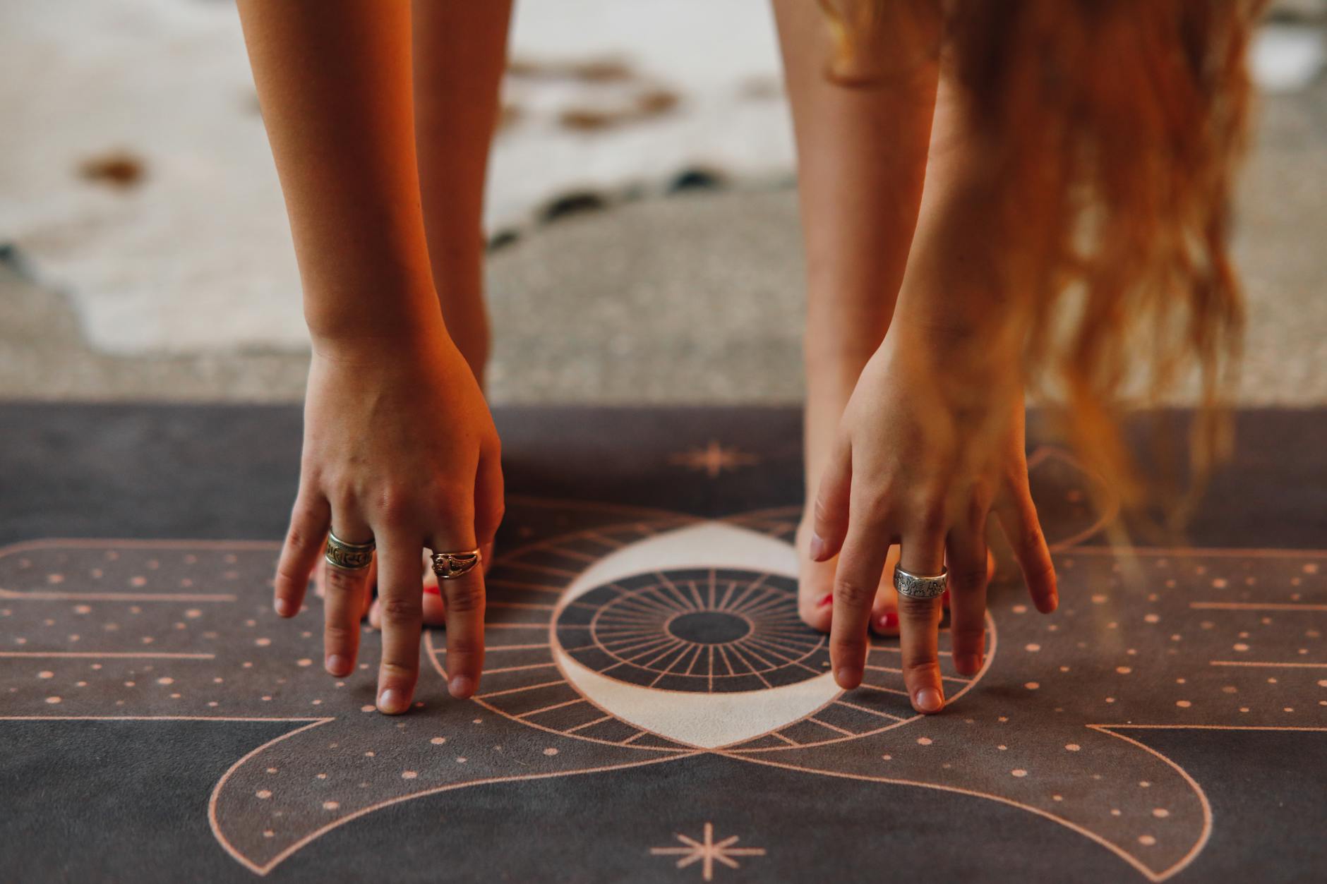 Detailed view of hands with rings in yoga pose on a decorative mat.
