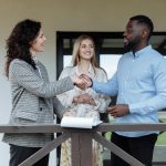 Three adults sealing a real estate deal with a handshake on a porch.