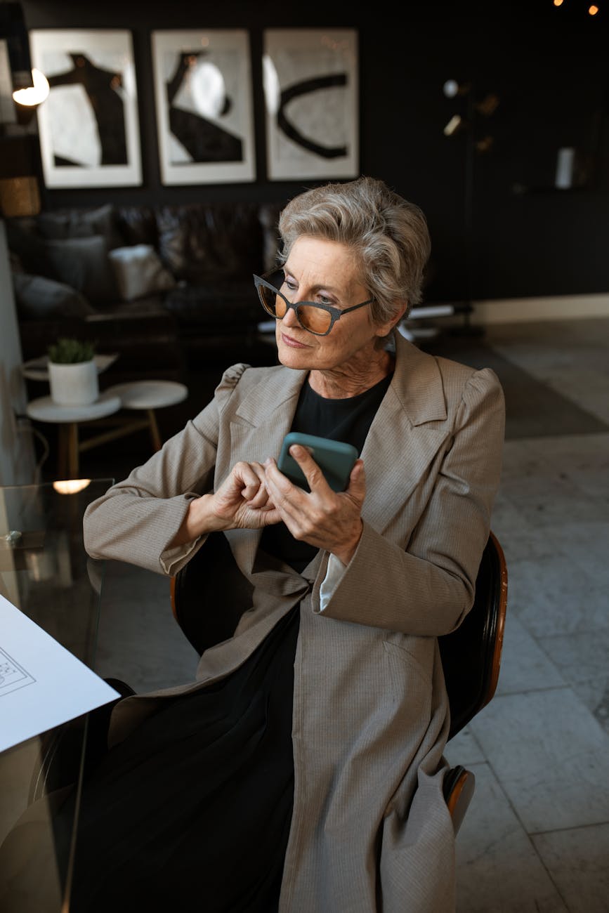 Senior woman using smartphone in a modern, stylish home office setting with chic interior design.
