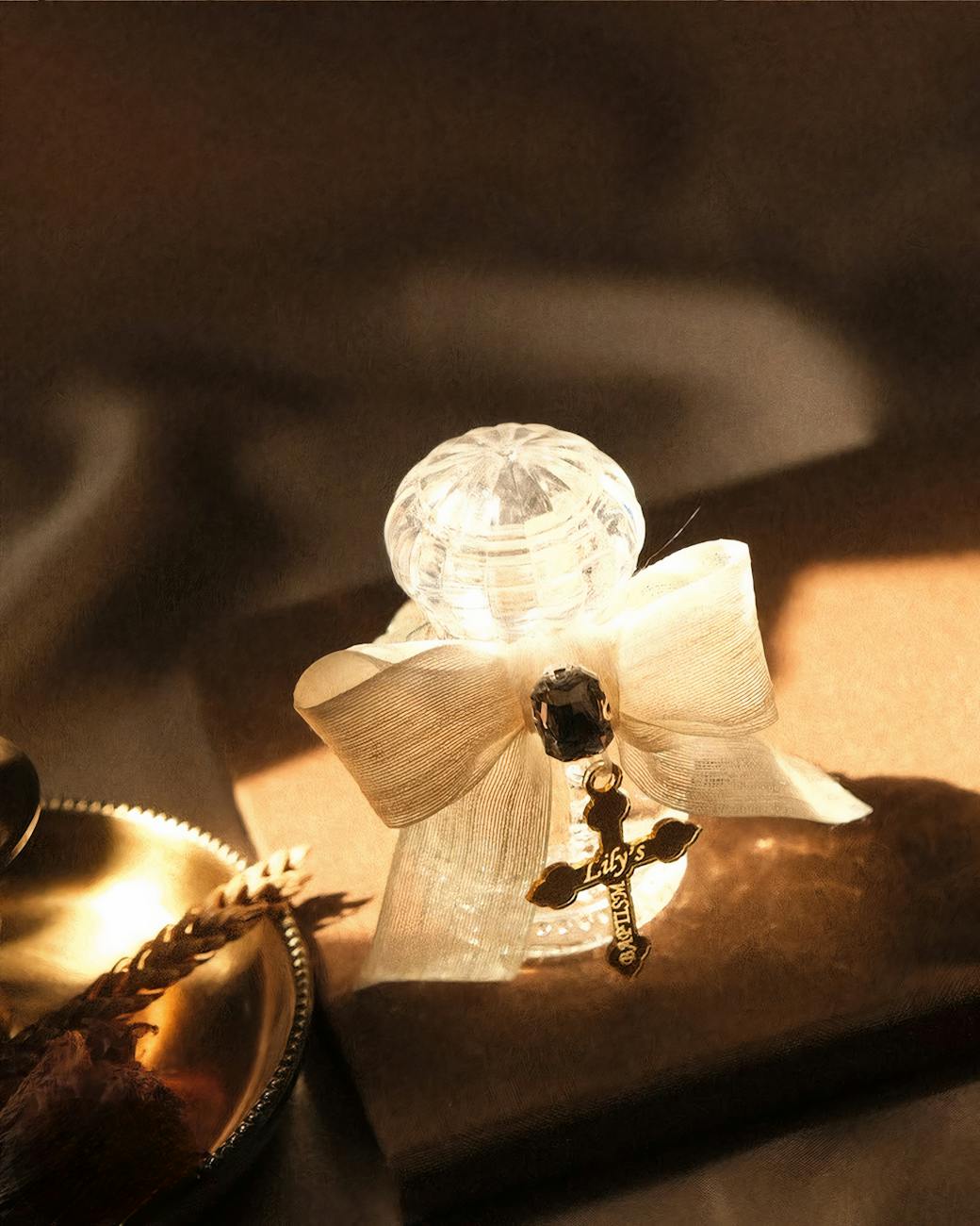 Glass perfume bottle adorned with a bow and charm, set in warm lighting.