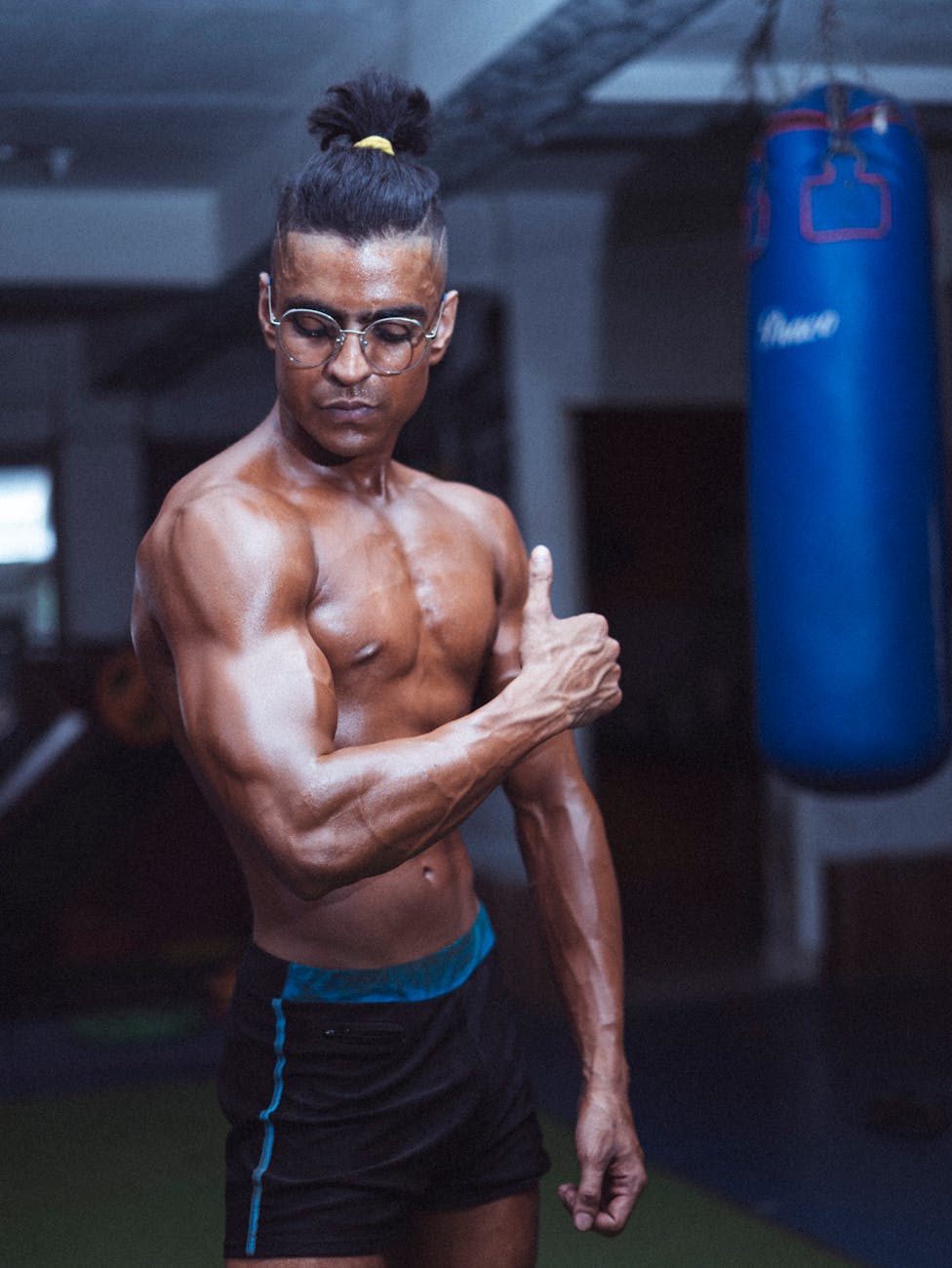 Muscular man flexing in gym with punching bag, showcasing strength and fitness.