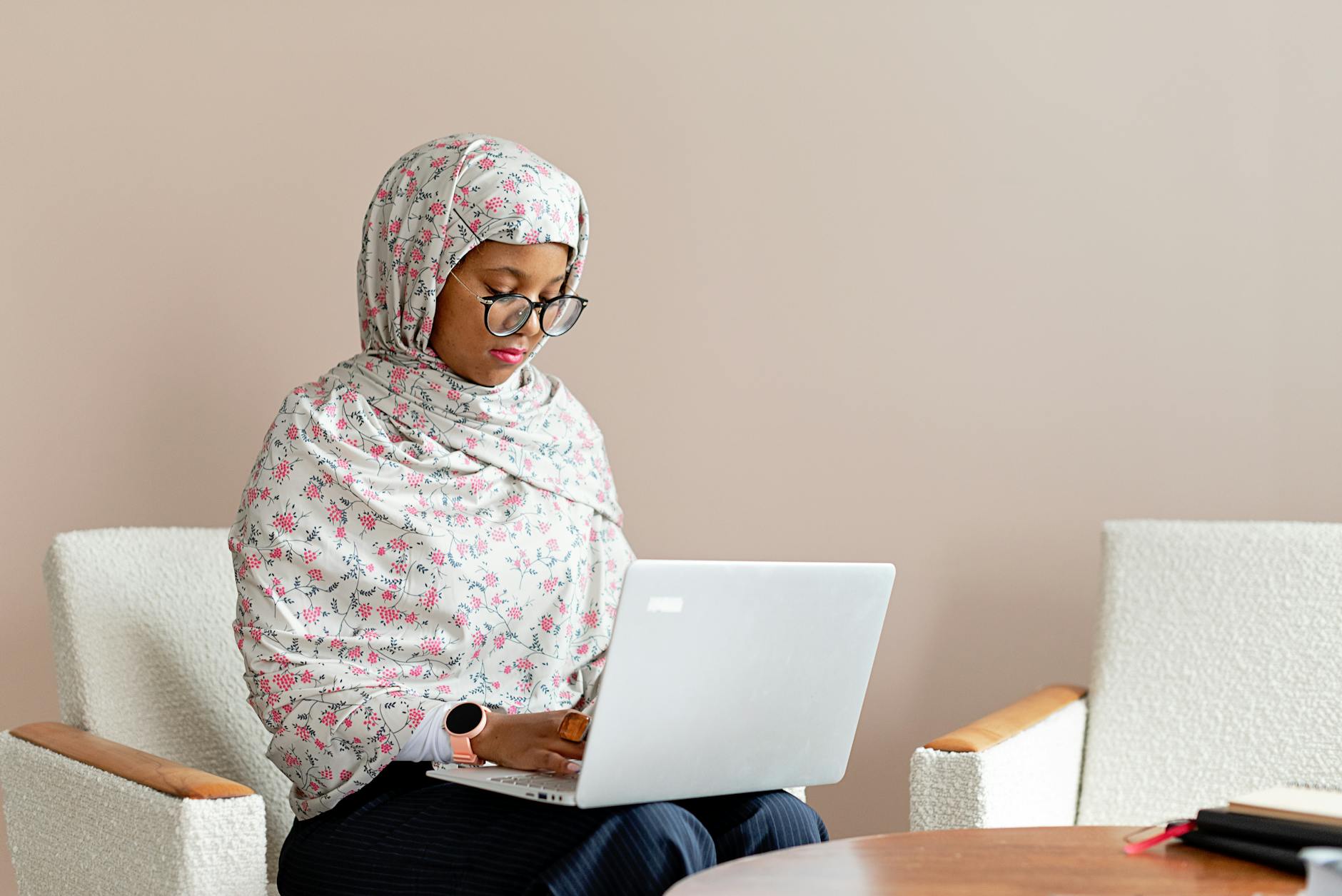 Focused woman in floral hijab using a laptop indoors, working on a project.