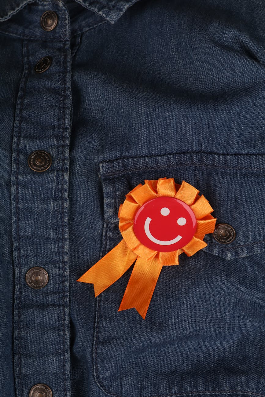 Close-up of a denim jacket featuring an orange ribbon with a red smiley face pin.
