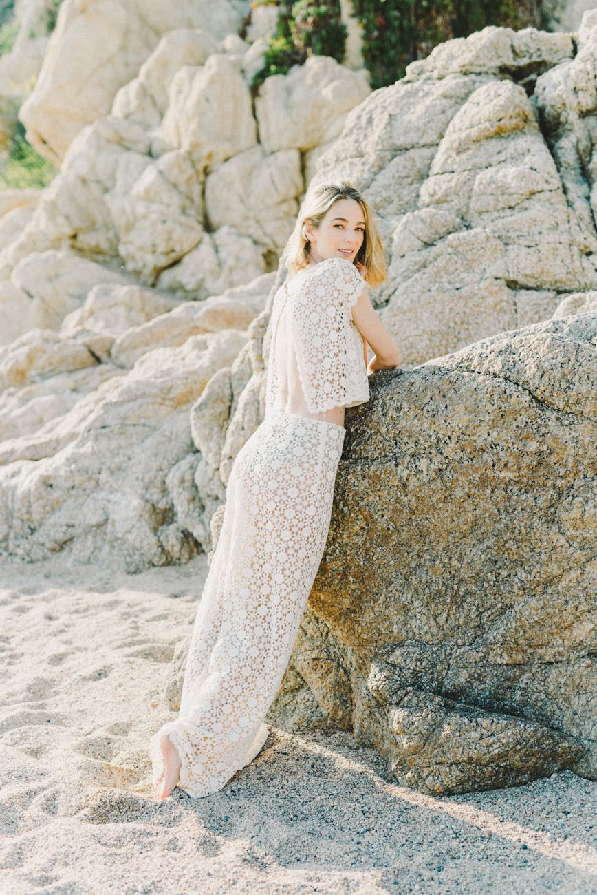 Woman in a jumpsuit posing on the rocky seashore, looking back with elegance.