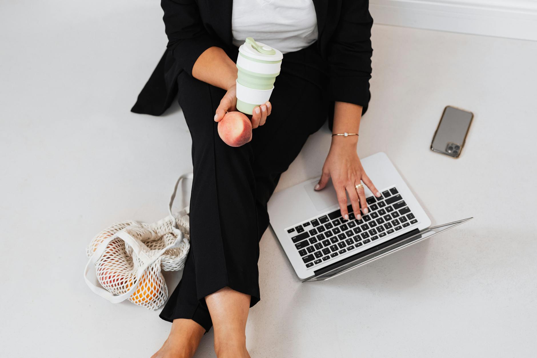 Businesswoman seated with laptop, peach, and reusable tumbler, representing work-life balance.