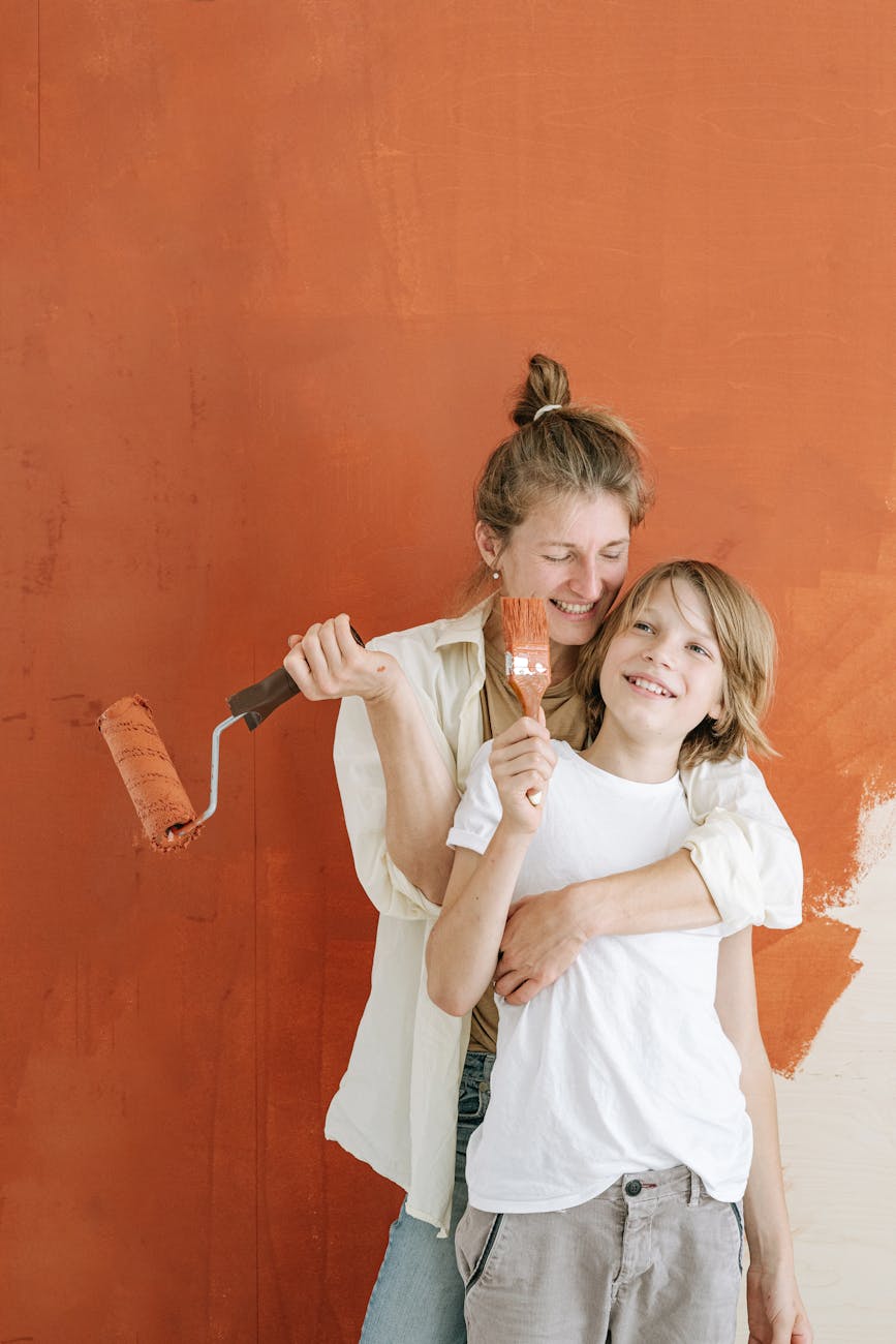 A joyful mother and son bonding while painting a wall together indoors.