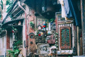 A cluttered, rustic outdoor workshop area with hanging clothes and vintage items scattered around.