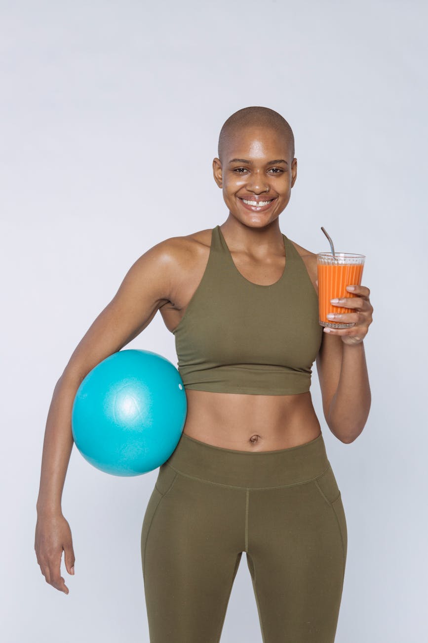 Fit woman smiling with a smoothie and exercise ball in studio.