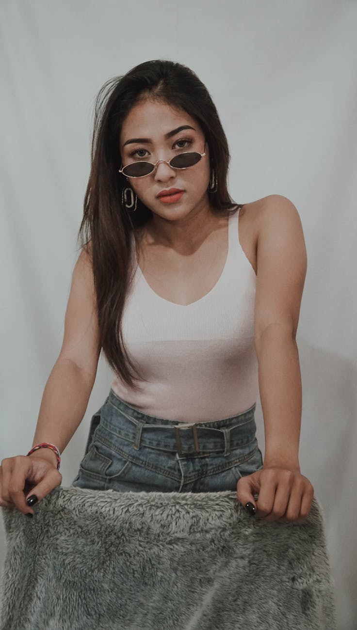 Fashionable woman wearing sunglasses poses with a confident attitude indoors.