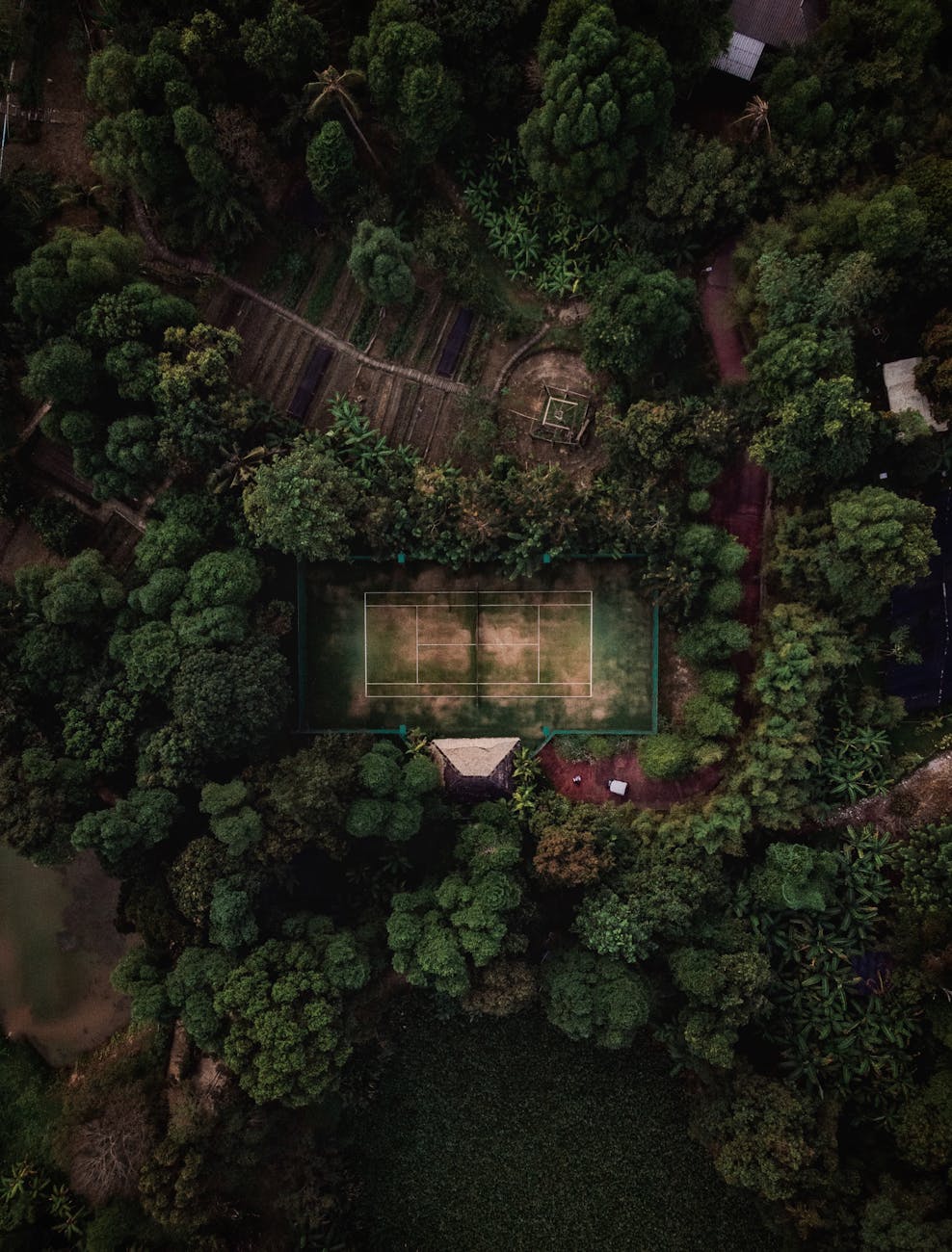 Drone shot of a tennis court nestled within a dense forest in Thailand, showcasing natural beauty.