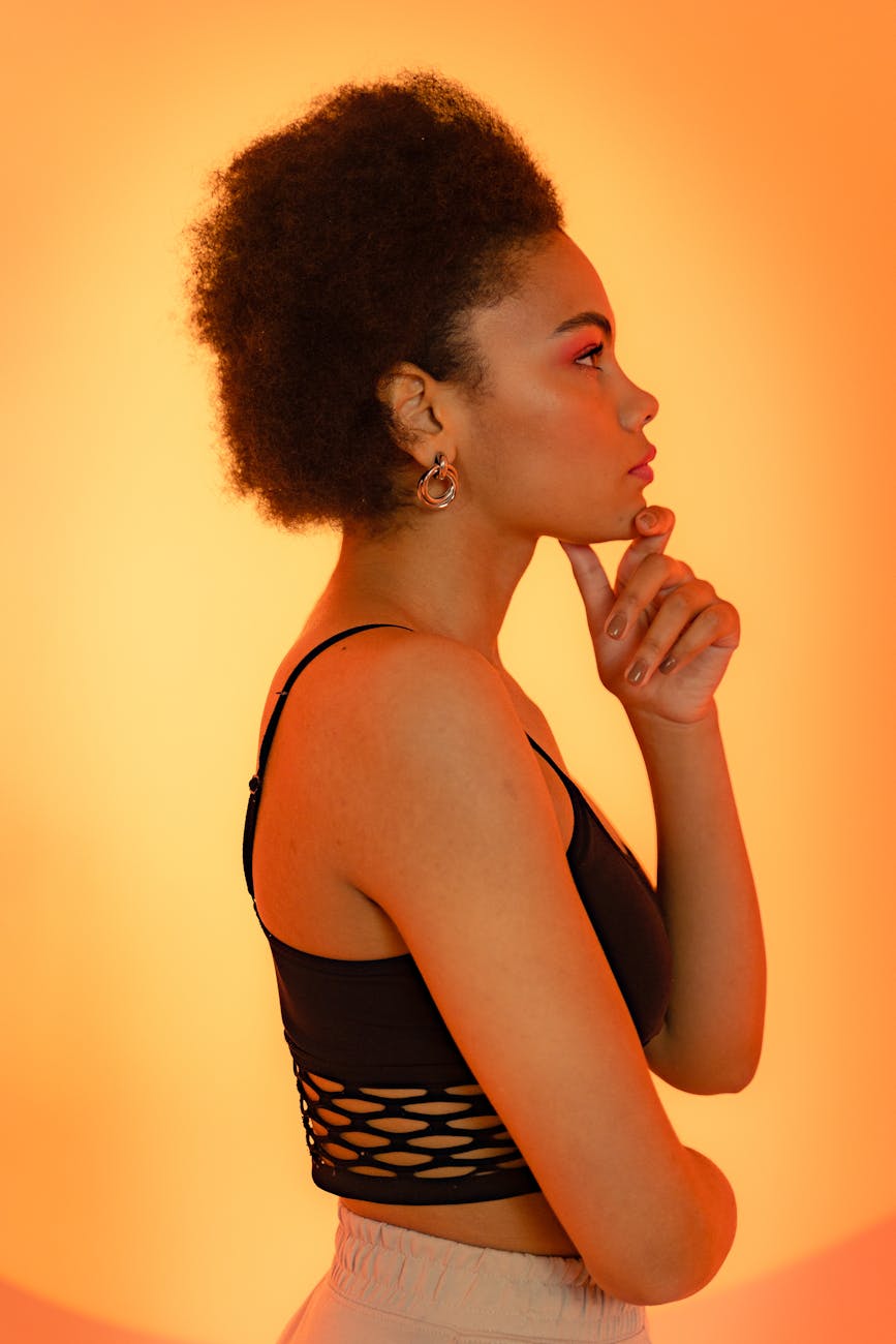 Side profile of a fashionable woman with afro hair posing in a studio with an orange background.