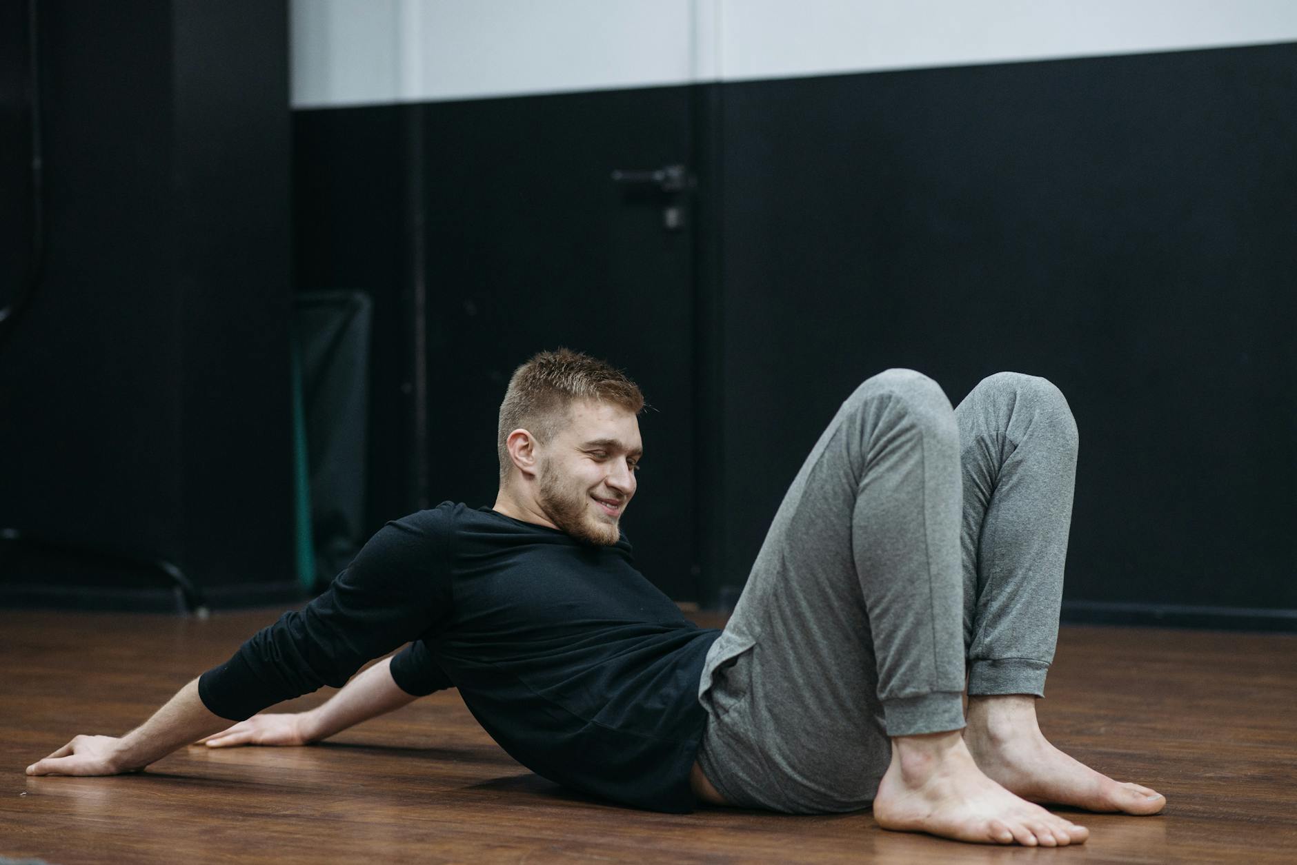Young man performing a stretching and relaxation exercise on a gym floor.