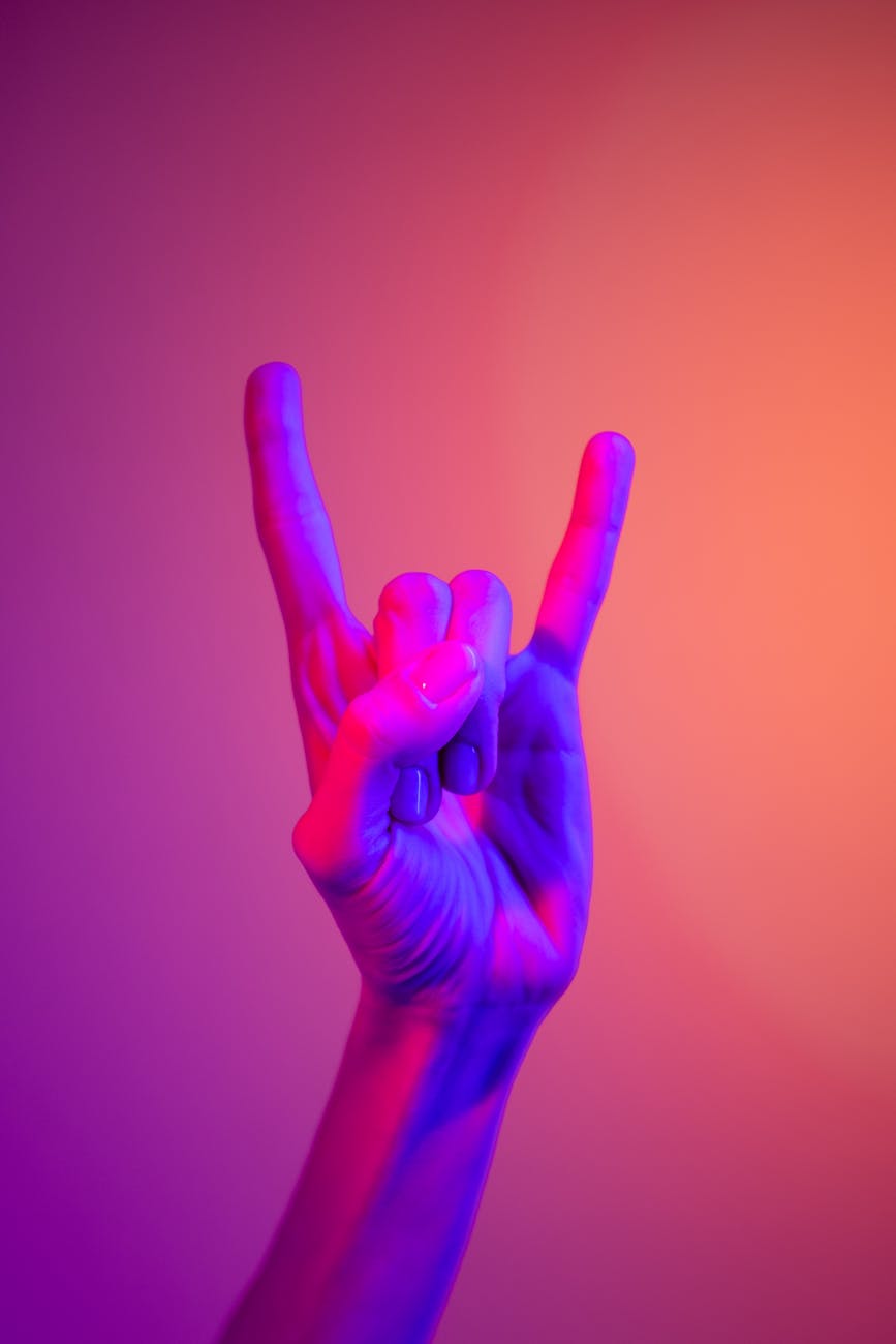 A hand showing the rock sign in vibrant neon colors, against a gradient background.