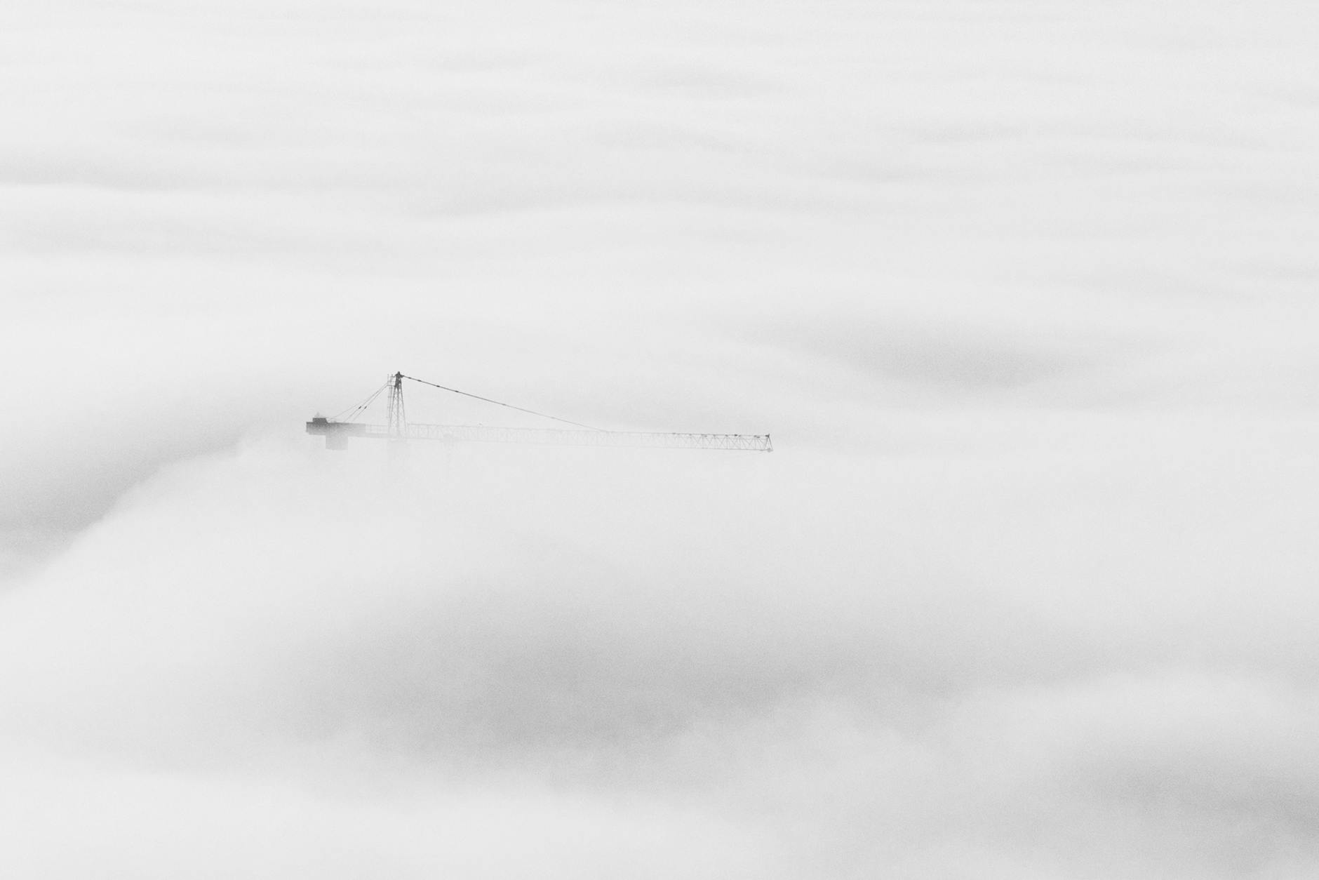 Ethereal view of a crane breaking through dense fog in Dubai, showcasing urban construction.