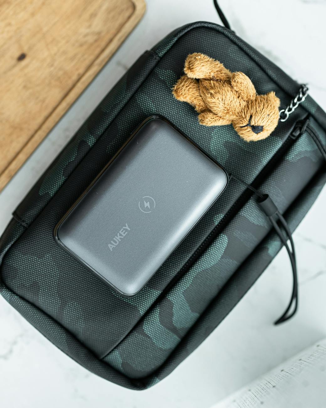 Close-up of a camouflage bag with a power bank and teddy bear keychain charm.